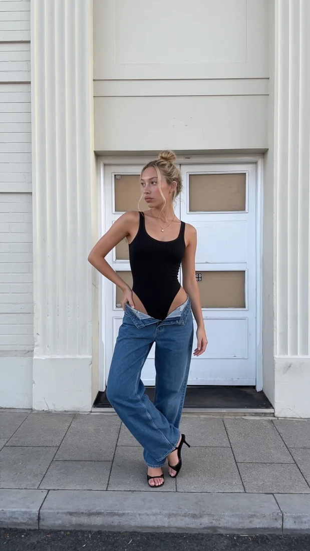 Avatar one standing on a city sidewalk in a black bodysuit and jeans